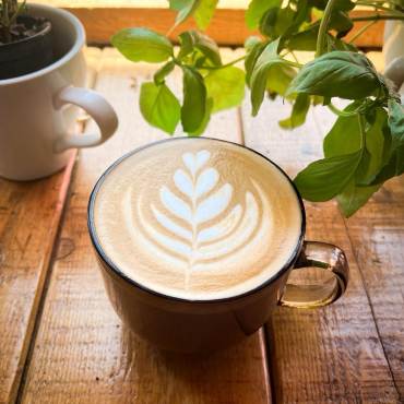 Un café con leche en una taza de café sobre una encimera de madera; tiene un dibujo de espuma con forma de espiga de trigo.