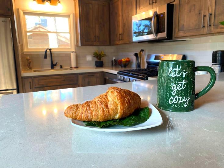 Una foto del interior de la cocina de una cabaña en la que se ve un cruasán sobre la encimera, junto a una taza verde; la cocina y el fregadero aparecen desenfocados.