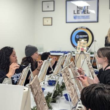 Un grupo de pintores aprendiendo a dibujar paisajes naturales, la profesora está de pie y les guía mientras continúa.