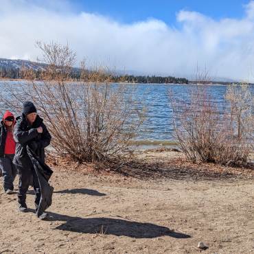 Un par de voluntarios abrigados escanean la orilla del lago Big Bear en busca de basura para limpiar como parte de los esfuerzos de Care For Big Bear.