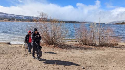 Un par de voluntarios abrigados escanean la orilla del lago Big Bear en busca de basura para limpiar como parte de los esfuerzos de Care For Big Bear.