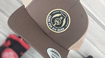 Gorra snapback de color marrón rojizo con el logotipo de Care For Big Bear bordado en la parte delantera, los lados de la gorra son de color tostado.