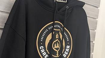 La sudadera, negra y con capucha, lleva el logotipo de Care For Big Bear que reza "Preservemos nuestro parque infantil natural".
