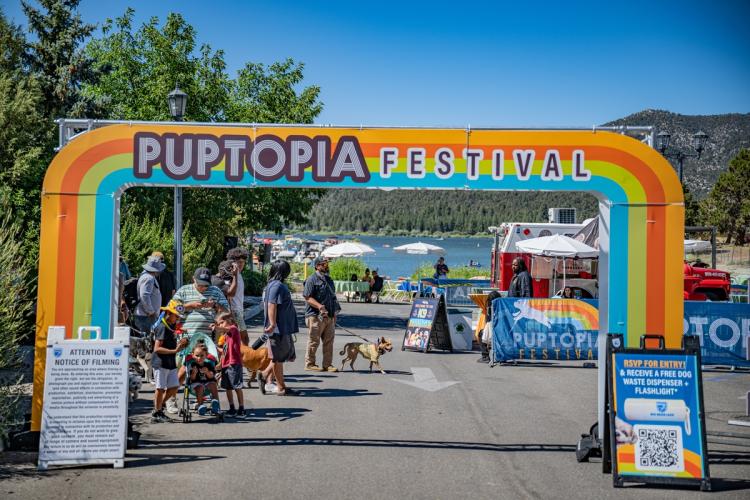 La entrada del evento Puptopia con un fondo de gente y sus perros, así como el lago a lo lejos.