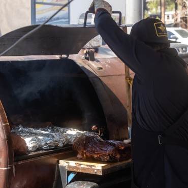 Un chef abriendo la puerta de una gran barbacoa y mostrando numerosas piezas de carne envueltas en papel de aluminio durante el Big Bear Grill & Chill.