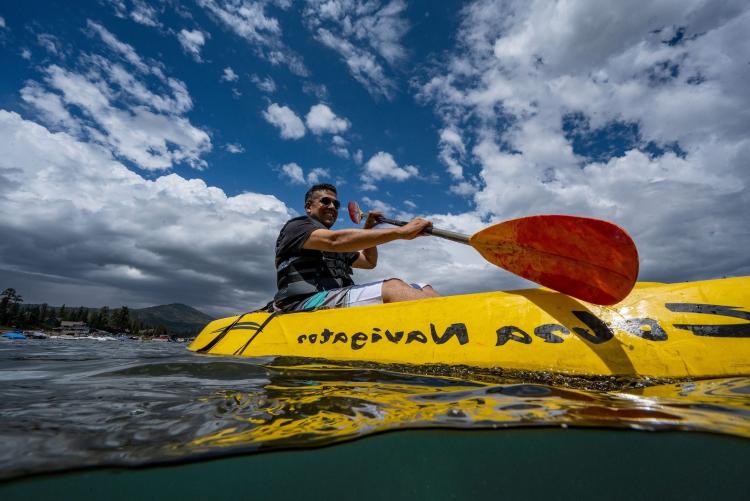 Un hombre sonríe mientras rema en un kayak amarillo en el lago Big Bear.
