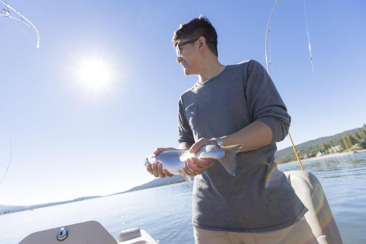 un hombre sostiene una trucha recién pescada mientras pesca en un día soleado en Big Bear Lake
