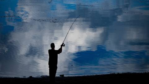 La silueta de un pescador se encuentra en la orilla del lago Big Bear y lanza un sedal al agua. El agua es azul
