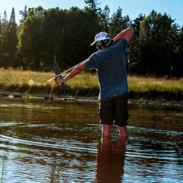 en un día soleado, un cazador se sitúa en el lago Big Bear y apunta con un arco y una flecha al agua durante el Carp Round-Up