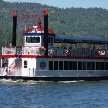 El barco de dos pisos Miss Liberty Paddlewheel navega por el lago Big Bear en un día soleado. Está pintado de rojo, blanco y azul.