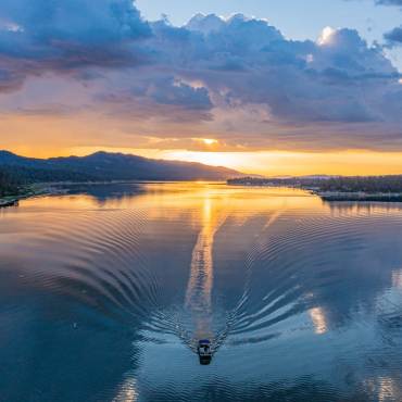 El lago Big Bear durante un amanecer de un resplandeciente color amarillo anaranjado; se ve una embarcación que deja una estela en el agua a su paso.