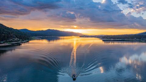 El lago Big Bear durante un amanecer de un resplandeciente color amarillo anaranjado; se ve una embarcación que deja una estela en el agua a su paso.