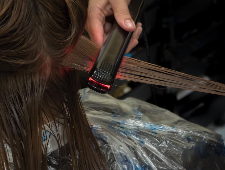 A photo of a lady having her hair being styled at a hair salon with a heated roller.