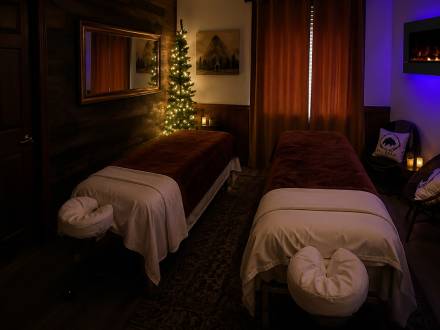 Dos camillas de masaje largas en una sala suavemente iluminada con luz ambiental; las camillas cuentan con fundas mullidas y reposacabezas.