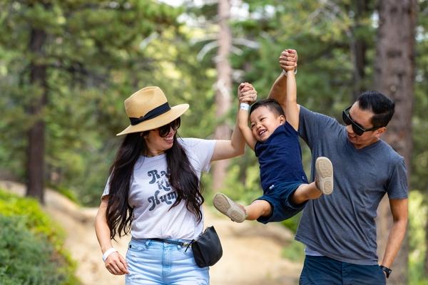Una foto de una familia haciendo senderismo mientras levantan juguetonamente a su hijo.
