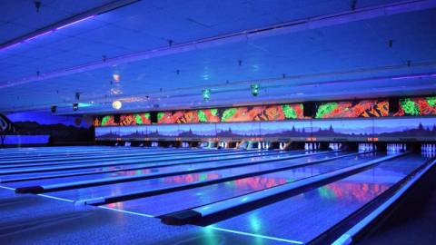 Luces de neón azules iluminan las pistas interiores de la bolera Big Bear Bowling Barn durante los eventos de bolos brillantes.