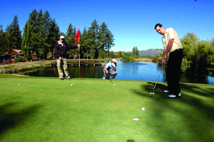 Un jugador de golf juega al putt en el green. Un hermoso lago azul en el campo refleja el cielo azul brillante.