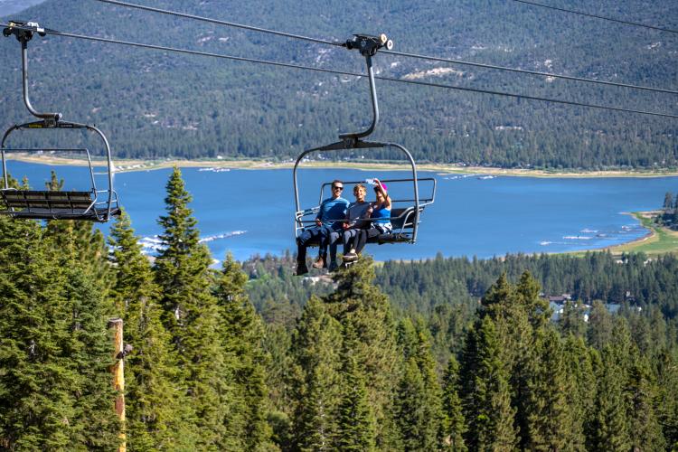 Una familia de tres miembros disfrutando de un paseo en la Sky Chair con vistas al hermoso lago Big Bear y el valle al fondo.