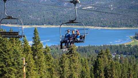 Una familia de tres miembros disfrutando de un paseo en la Sky Chair con vistas al hermoso lago Big Bear y el valle al fondo.