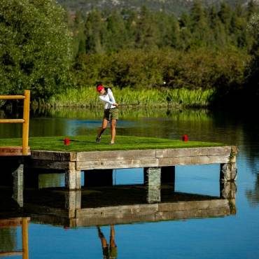 Una foto de una señora en medio de un columpio en el campo de golf Bear Mountain, la plataforma bajo ella está flotando sobre un estanque.