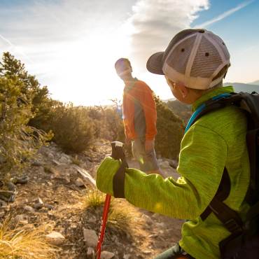 Una foto de un hijo y su padre haciendo senderismo en una montaña justo antes de la puesta de sol.