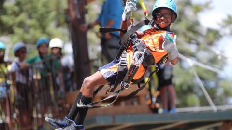 Una foto de un niño atado firmemente para hacer tirolesa con Action Zipline Tours, lleva guantes gruesos y casco.