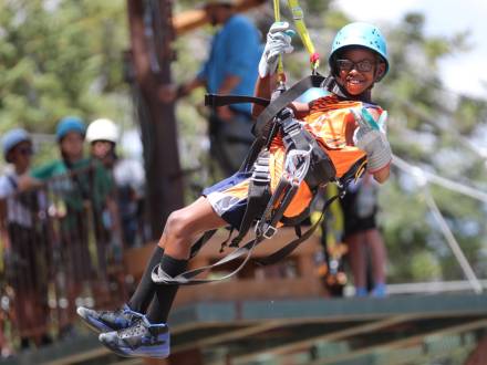 Una foto de un niño atado firmemente para hacer tirolesa con Action Zipline Tours, lleva guantes gruesos y casco.