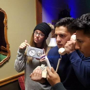 Tres amigos -uno con un reloj y otro con un teléfono- resuelven su salida de una sala de escape en Big Bear Lake, CA