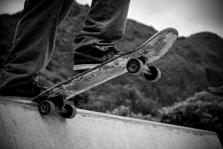Foto en blanco y negro de una persona montando en monopatín al borde de un pequeño muro, con las montañas visibles a sus espaldas.