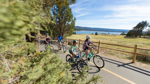 Una foto de una familia de cuatro miembros montando en bicicleta por una carretera estrecha, con el lago Big Bear visible a lo lejos.