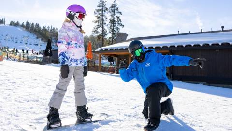 Un instructor guía a un alumno sobre una tabla de snowboard en la estación de esquí Snow Summit de Big Bear Lake, California.