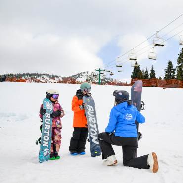 Foto de dos jóvenes snowboarders aprendiendo a hacer snowboard con un instructor en la estación de esquí de Bear Mountain.