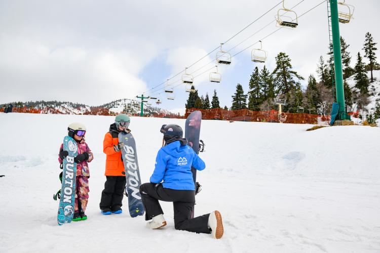 Foto de dos jóvenes snowboarders aprendiendo a hacer snowboard con un instructor en la estación de esquí de Bear Mountain.