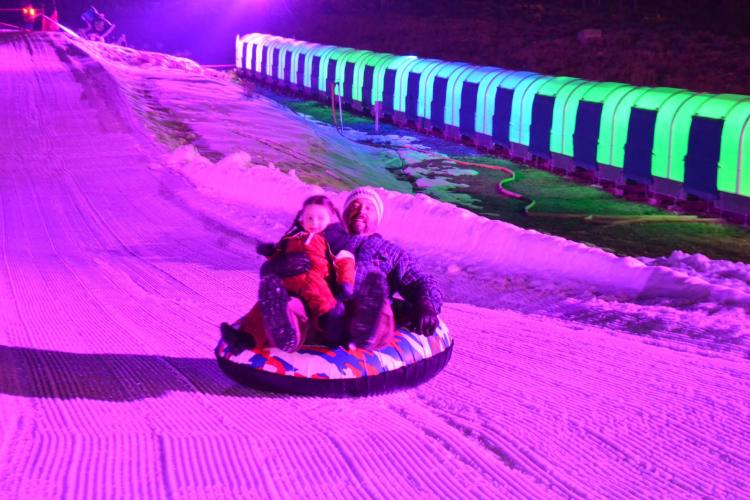 Un padre y su hijo se deslizan por la colina de tubing durante Glow Tubing en Big Bear Lake.