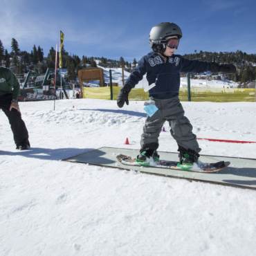Un joven snowboarder se desliza por una barandilla durante una clase. Su instructor lo observa.