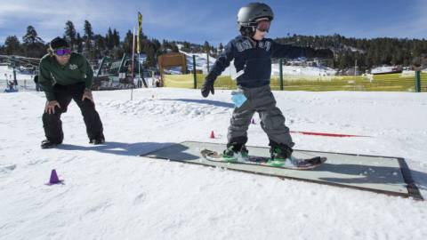 Un joven snowboarder se desliza por una barandilla durante una clase. Su instructor lo observa.