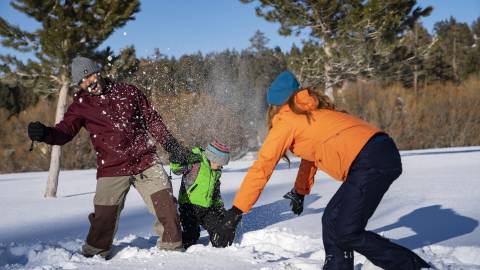 Una familia de tres miembros juega en la nieve durante el invierno en Big Bear Lake.