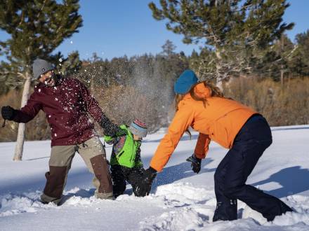 Una familia de tres miembros juega en la nieve durante el invierno en Big Bear Lake.