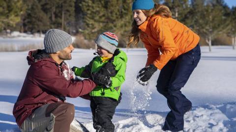 Una mamá y un papá juegan con su hijo en Big Bear durante el invierno. La nieve cubre el suelo y todos sonríen.