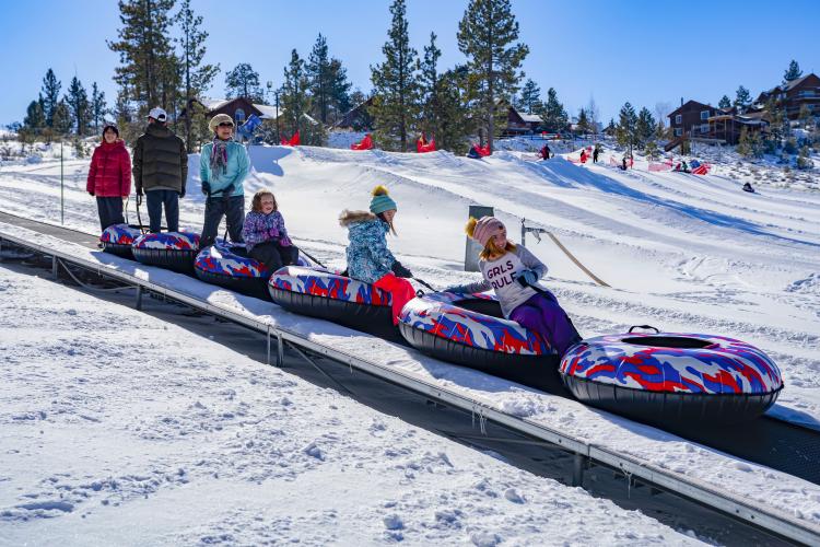 Una familia sube a una alfombra móvil para disfrutar de los juegos de nieve en Big Bear. Llevan tubos de nieve de colores brillantes.