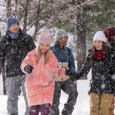 Un grupo de cuatro personas abrigadas en la nieve, con copos cayendo a su alrededor y árboles verdes detrás de ellos.