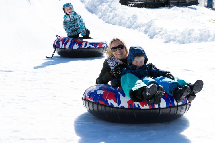 Una madre y su hijo se deslizan por una colina nevada mientras practican tubing en Big Bear Lake en invierno.
