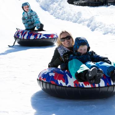 Una madre y su hijo se deslizan por una colina nevada mientras practican tubing en Big Bear Lake en invierno.