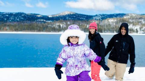 Una niña, abrigada con ropa de nieve, camina por la nieve delante de sus padres durante el invierno en Big Bear Lake.
