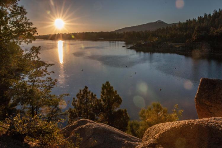 Una foto del lago Big Bear, con la puesta de sol iluminando suavemente el lago y las montañas, y el agua reflejando la playa como un espejo