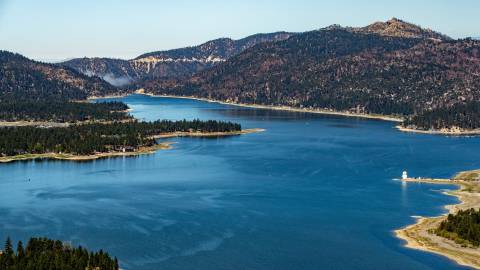 Una vista aérea del lago Big Bear. Es un día soleado, con cielos azules despejados y verdes pinares rodean el lago azul.