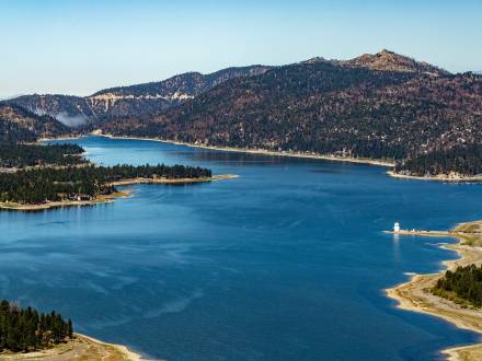 Una vista aérea del lago Big Bear. Es un día soleado, con cielos azules despejados y verdes pinares rodean el lago azul.