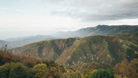 A photo of tall lush green mountains, the gray clouds providing some shade from above.