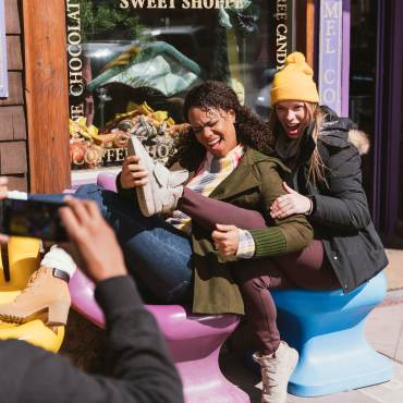 Un hombre hace una foto a dos mujeres que posan sentadas en las sillas de estilo manual de la tienda Village Sweet Shop.