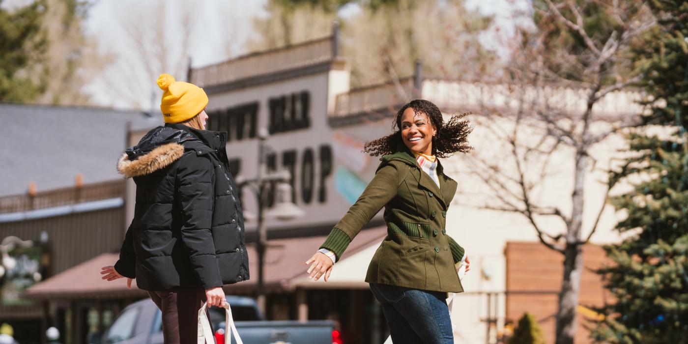 Un par de señoras cruzan la carretera en el pueblo de Big Bear Lake, una de ellas lleva una bolsa de Bear Cupboards Market.